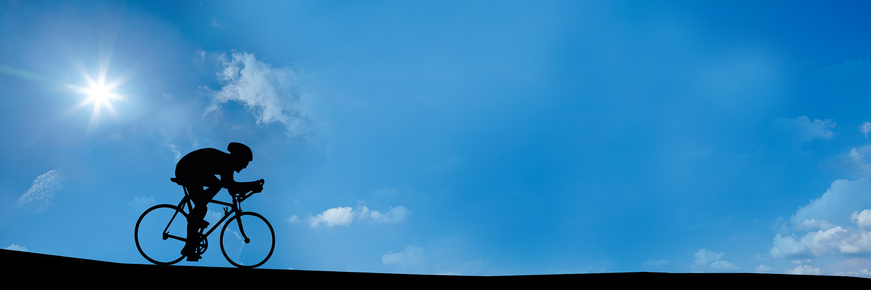 A male cyclist riding along a road in sunshine